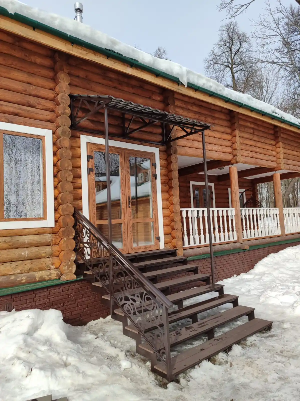 Уличная лестница с кованым ограждением у сруба зимой в снегу